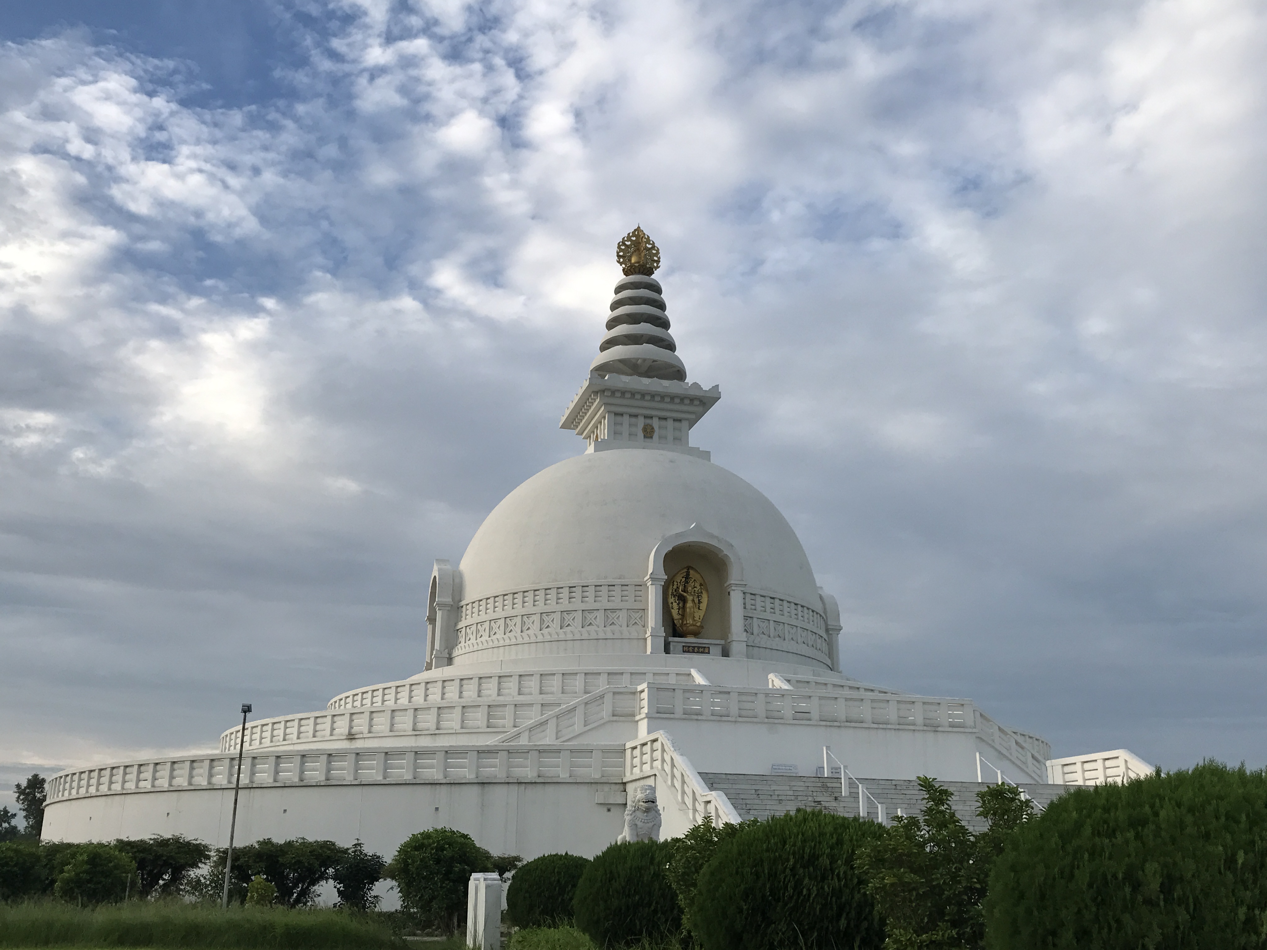 An image of the World Peace Pagoda in Pokhara, Nepal, a gleaming white stupa perched on a hilltop overlooking Phewa Lake, surrounded by lush greenery and the Annapurna mountain range in the background.