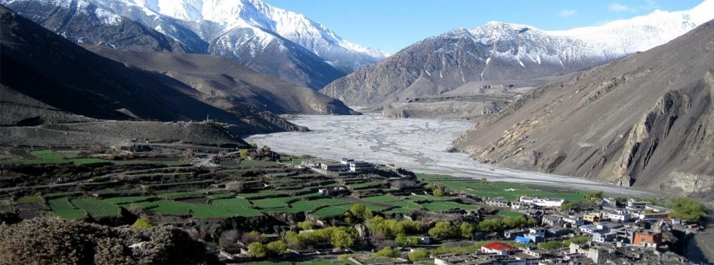 A stunning aerial photograph depicts the rough and desolate environment of the Dolpo to Mustang trip, exhibiting towering cliffs, vast valleys, and snow-capped peaks against an unending blue sky.