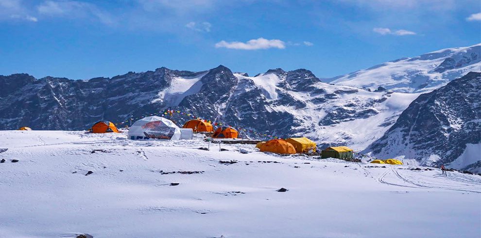 The Rupina La Pass Trek, known for its untamed beauty and high-altitude adventures, is vividly depicted in this alluring image. The meandering trails of the hike, carved into the jagged mountainside, direct the gaze towards an incredible view of distant, snow-capped peaks. The vast blue skies above provide the ideal backdrop for the unbroken peace of this remote path. The sparse foliage lends a touch of life and demonstrates how resilient nature is in such hostile environments. This image perfectly captures the unadulterated wilderness, unbridled beauty, and attraction of exploration that define the Rupina La Pass Trek.