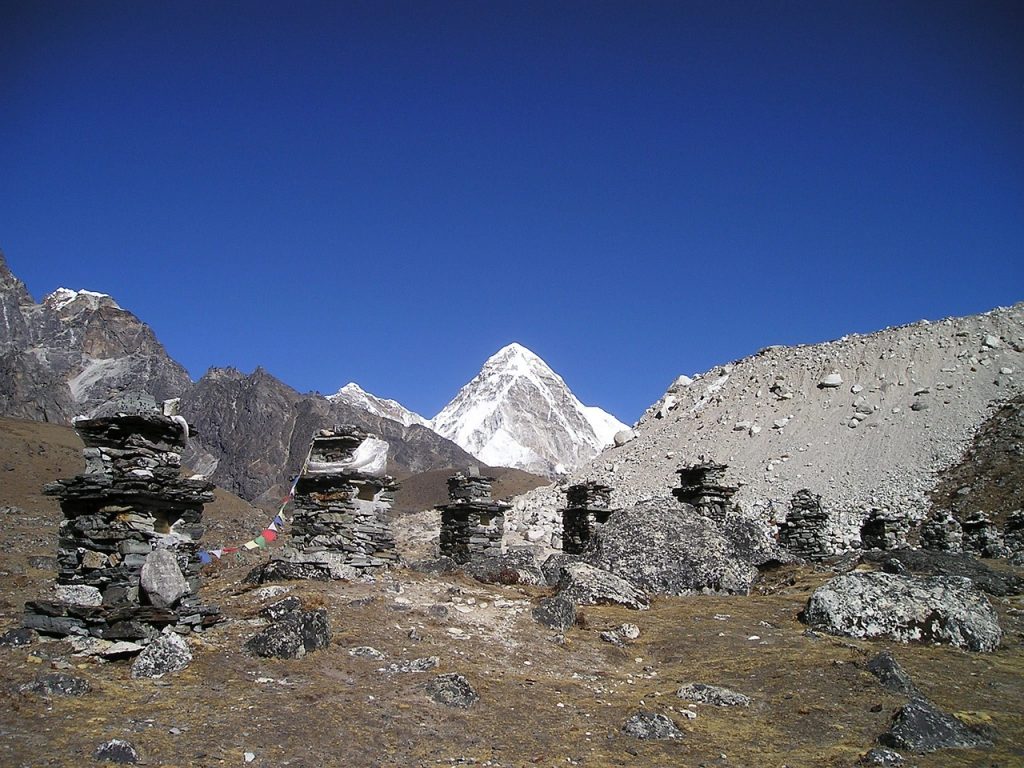 An image depicting the grand Puomri mountain rising majestically in the distance, with a complex Buddhist stone sculpture occupying the foreground and center, symbolizing the region's long spiritual history.