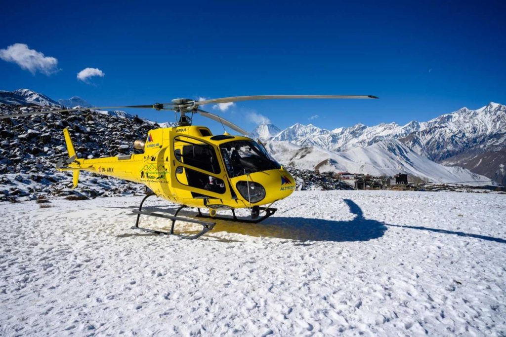 Helicopter flying above the Annapurna region's harsh terrain, with snow-capped peaks in the distance.