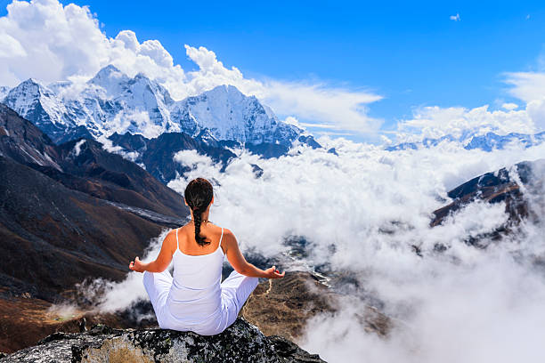 Practitioner striking a yoga pose on a rocky outcrop with the snow-capped peaks of Mount Everest and surrounding mountains in the serene background.