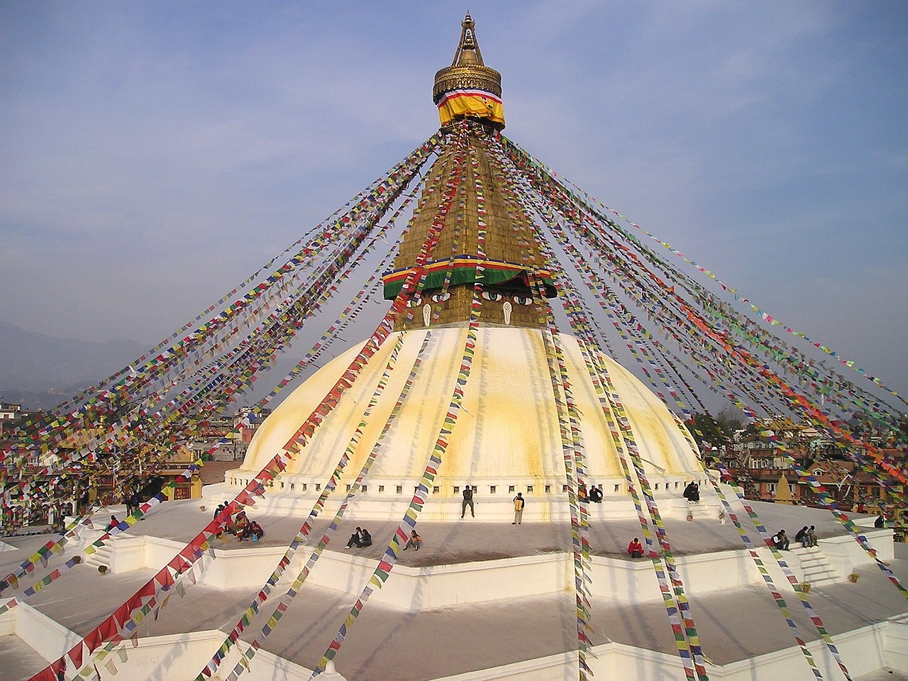 The Boudhanath Stupa is depicted in this iconic artwork with a backdrop of a blue sky, a large mandala, a white dome, and a golden spire topped with the all-seeing eyes of the Buddha.