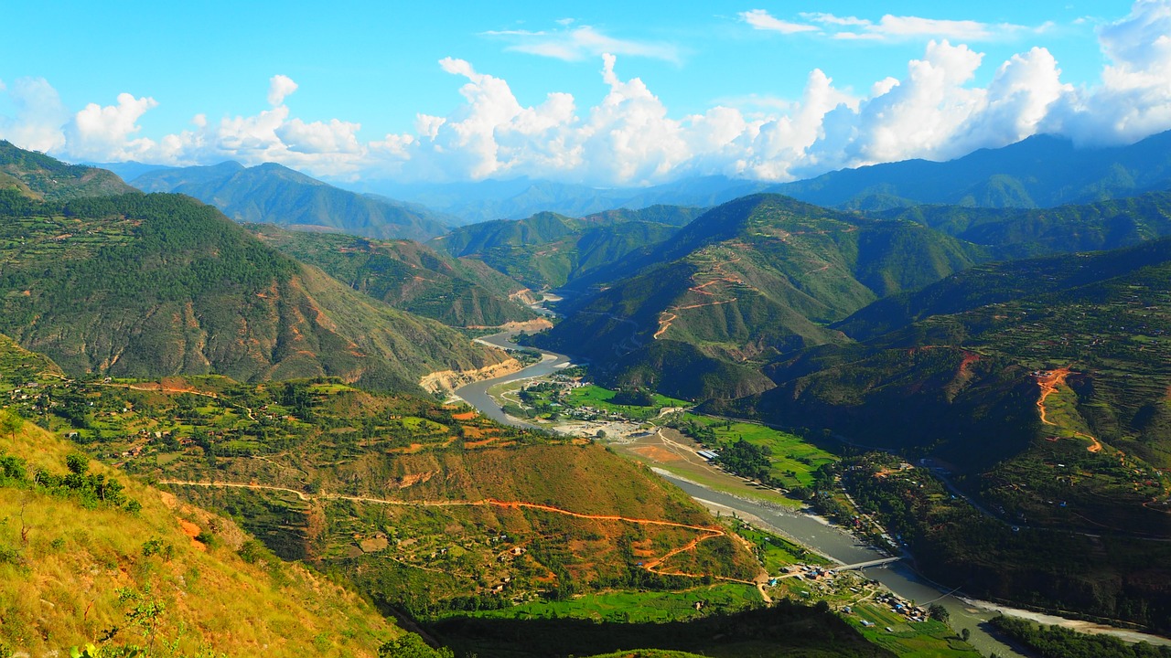 Panoramic view with rolling green hills in the foreground and towering mountain peaks in the background.