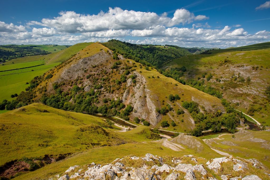 Rolling green hills of Ilam, adorned with terraced tea plantations, under a soft blue sky with fluffy clouds.