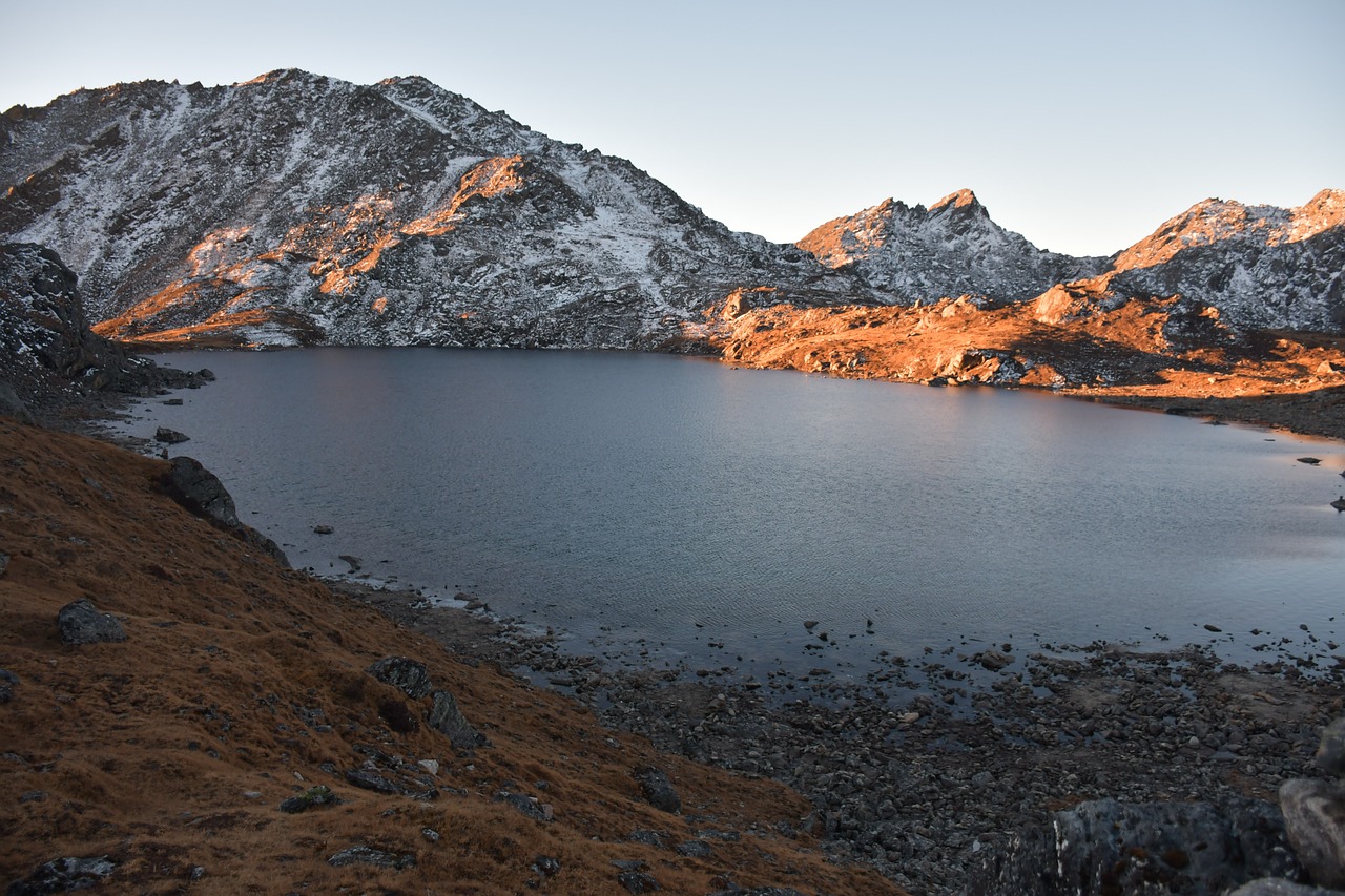 Elevated view of Gosaikunda Lake's azure waters, surrounded by rugged mountains with patches of snow, under a clear sky.