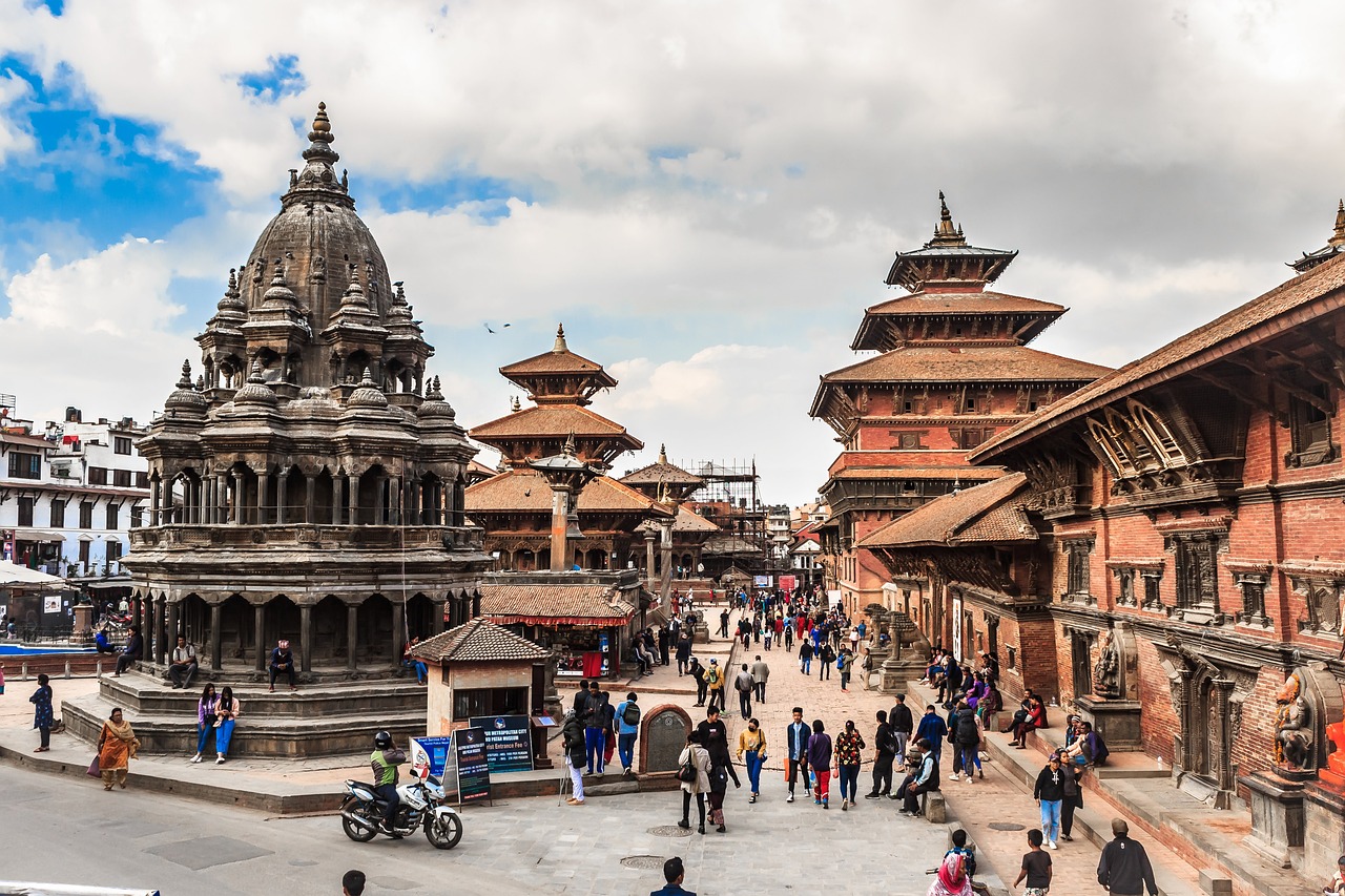 An image of Patan Durbar Square in Lalitpur, Nepal, featuring ancient temples, stone statues, and intricate Newari architecture under a vibrant sky.