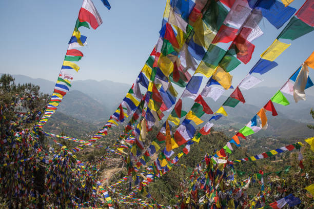 Colorful prayer flags fluttering in the wind on Dhulikhel Hills, with a scenic backdrop of lush greenery and distant mountain ranges.