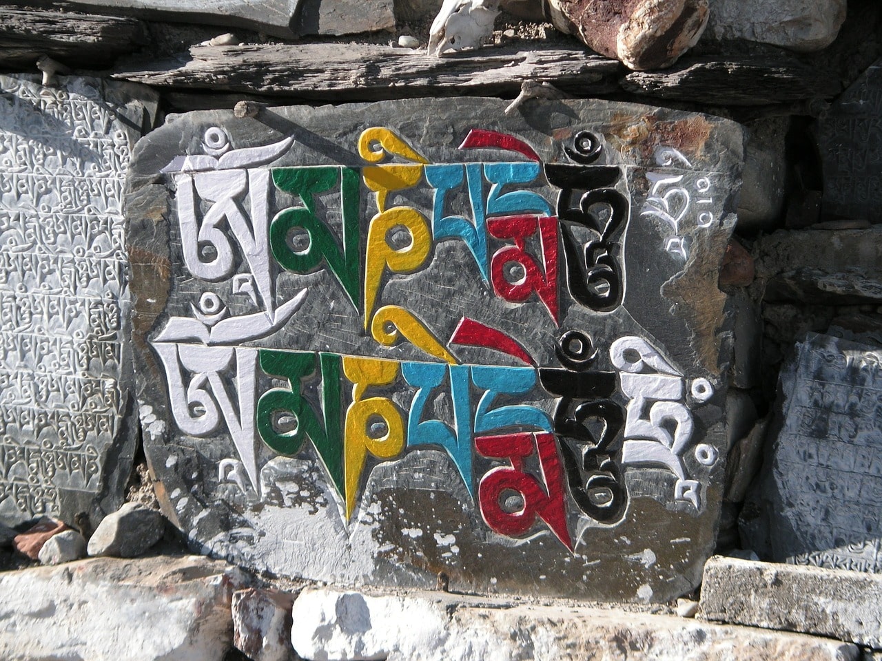 Colorful Tibetan mantra "Om Mani Padme Hum" carved on a mani stone with surrounding stone inscriptions.