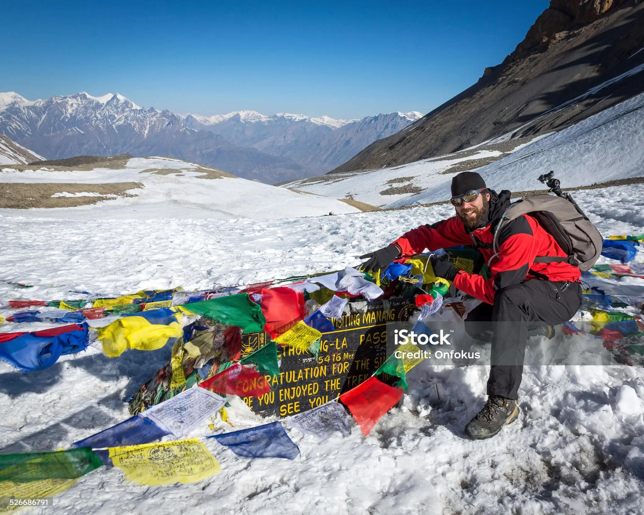 A trekker ties a prayer flag at the Thorong La Pass welcome board, marking the achievement of crossing one of the world’s highest trekking passes.