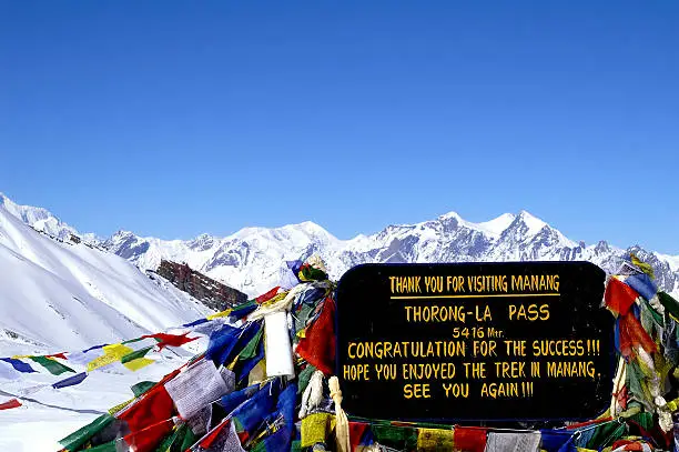 Thorong La Pass welcome board at 5,416 meters, the highest point of the Annapurna Circuit Trek with prayer flags fluttering.